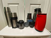 All six insulated drinkware items displayed including mugs and pitchers next to white double doors on a white table