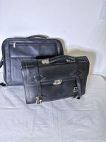 Shows front and angled view of vintage leather satchel with embossed logo and locking clasp in front of modern laptop case.