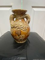 Front view of the beige and brown porcelain dragon vase on a black surface with a white door background.