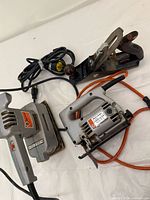 Photo showing Black & Decker jigsaw, finishing sander, and vintage hand plane together on a white surface, displaying overall condition and cords.
