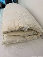 Folded white goose down duvet on bed, showing thickness and size.