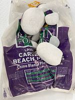 Large smooth white pebbles sitting on a partially opened purple and white bag labeled Caribbean Beach Pebbles by Rocks & Forests, showing size comparison and bag details.