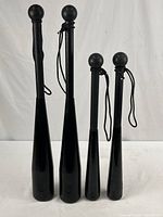 Front view of four black steel clubbells, two larger weighing 10 lbs and two smaller weighing 5 lbs each, standing upright with wrist straps visible.