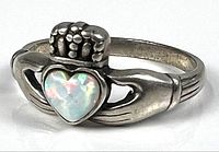 Close-up view of sterling silver ring featuring a synthetic opal heart stone set in a Claddagh design with detailed hands and crown