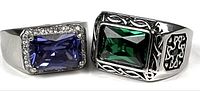 Two sterling silver rings side by side, one with a rectangular blue glass stone framed by clear stones, the other with a large rectangular green glass stone and ornate filigree design on the band.