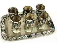 Photo showing six silver metal cordial cups arranged on a rectangular tray with iridescent inlay on edges and cup sides.