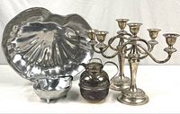 Photo showing all six items: two silverplate candelabras with floral detailing, a lidded pitcher, and two scalloped silver tone serving dishes.
