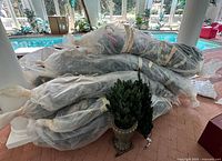 Stacked large artificial Christmas trees wrapped in plastic with one small potted tree visible