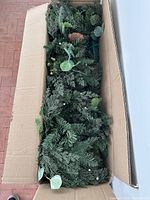 Open box showing artificial evergreen garland with integrated lights and mixed foliage