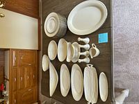 All items arranged on table including stacked dinner plates, platters, shakers, gravy boat