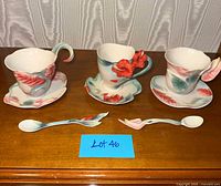 Full view of three sculpted floral teacups, saucers and spoons