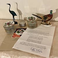 Full lot: two stacks of 3-inch songbird plates, cast iron stork, Lefton pheasant figurine, Franklin Mint paperwork