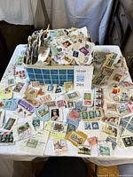 Top view of blue-pattern tin overflowing with assorted worldwide stamps spread on table