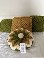 Front view of three square pillows (two green, one gold) and one round pillow