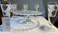 Front view of six pilsner glasses around clear cake plate on pedestal base