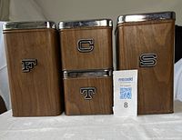 Front view of four metal canisters with F, C, T, S letters