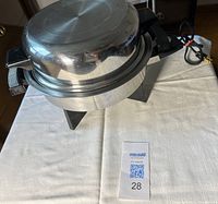 Frying pan inverted showing polished lid and base on cloth surface with cord attached