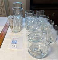 Assortment of 12 clear glasses arranged on table with ruler for scale