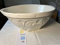 Side view of white stoneware bowl showing embossed motifs and fluted rim.