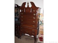 Full view of tall wooden chest with carved top and multiple drawers showing its overall structure and detailing.