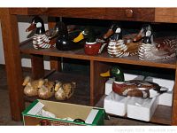 Eight carved wood ducks displayed on a wooden shelf, including five larger mallard style ducks and three smaller light brown ducks, plus one ceramic planter.