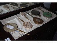 Overview of all five hand mirrors and one hairbrush displayed on a white embroidered cloth on a dresser.