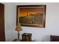 Framed wall art and brass desk lamp on side table with wicker cabinet underneath painting.