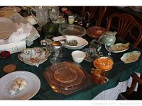 Top view of assorted glassware, china, and dishware spread on a dark tablecloth including floral china piece, amber glass candy dish, clear and green glass pieces.