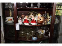 Wide view of the cabinet shelf showing all the items including yellow depression glass and ceramic figurines.