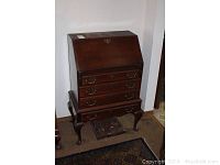 Front view of a dark wood ladies writing desk with drop-front closed, featuring brass hardware and cabriole legs.