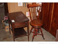 Side view of the antique end table and carved piano stool side by side, showing drawer and lower shelf on table and seat/back detail on stool.