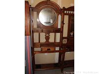 Full view of the wood hall tree with round mirror, hooks, and shelf under mirror.