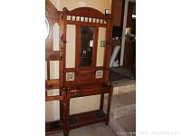 Full view of tall wooden hall tree with mirror and storage features in corner near stairs.