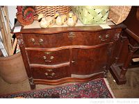 Front view of antique wooden dresser showing curved drawers, central cabinet door, brass hardware, and carved details.
