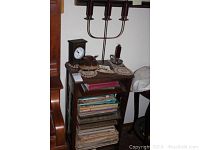 Full view of wood sheet music shelf with multiple shelves holding assorted sheet music, small clock, wood fish piece, and candelabra on top.