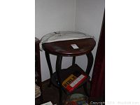 Antique round wooden table with curved legs and half cloth cover, lower shelf visible holding books and puzzle