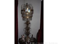 Full view of the tall brass and crystal chandelier lamp with decorative tiers of hanging crystals, standing on a table with other items around it.
