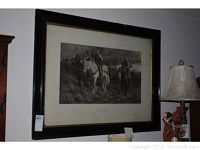 Full view of framed Joan of Arc engraving on wall with visible frame damage and adjacent lamp.