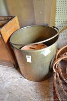 Full view of large brass bucket showing overall size and shape, placed on the floor with wooden slats inside.