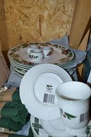 Stack of plates and three small cups showing the front design with leaves and berries.