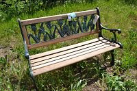 Front view of outdoor garden bench showing wood slats seat and decorative cast metal backrest with foliage pattern.