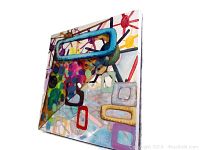 Angled close-up view of the square acrylic painting showing the colorful geometric shapes and layered patterns.