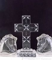 Full view of the clear crystal cross sculpture centered with two clear glass horse head bookends on each side, black background.