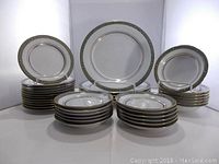 Photo showing multiple stacks of dinnerware including plates, bowls, and saucers with a decorative gold and gray border.