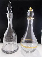 Two decanters on black background showing glass bell-shaped with etched pattern on left and crystal with gold trim on the right.
