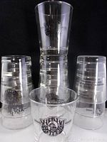 Set of 11 clear rocks glasses stacked and arranged with the Sports Page Club logo visible in black printing on each glass.