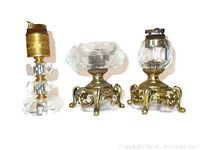 Full view of 2 brass and crystal lighters and 1 ashtray on ornate brass bases with cut crystal sections.