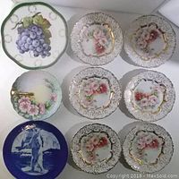 Photo showing nine decorative plates arranged in grid, highlighting floral, grape, and figure designs.