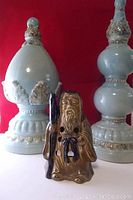 Front view of monk-shaped tea-light holder with two blue ceramic decorative ornaments against red background