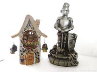 Two figurines side by side: the colorful cottage tea-light sculpture and the knight metal figurine.